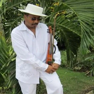 Man in white traditional attire holding a guitar in lush green tropical garden, wearing a wide-brimmed hat, representing musi