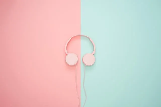 Pink and white headphones on a pastel split background, emphasizing music technology and digital media.