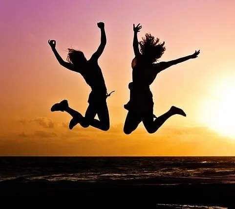 Two people jumping joyfully on the beach at sunset, celebrating fun and freedom during a summer evening.