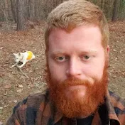 A man with a red beard outdoors, surrounded by trees and a bird flying nearby, enjoying nature and photography.