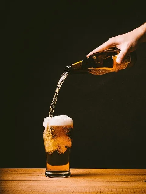 Bottle of beer being poured into a glass on dark background.