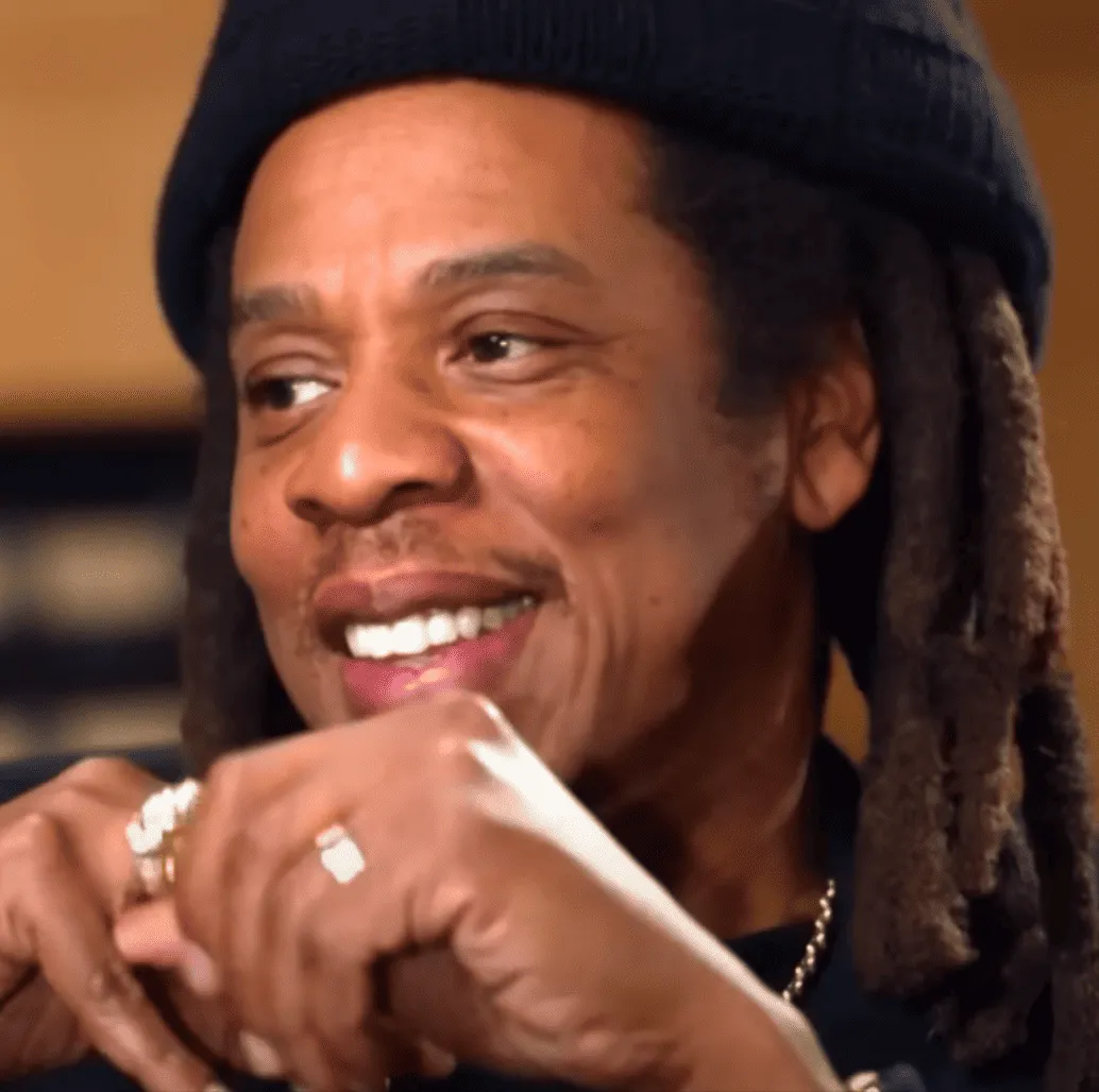 Man smiling with dreadlocks and rings, casual attire, music studio background, joyful expression, positive vibe, music indust