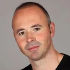 Image of a man with a friendly expression, bald head, and light skin, wearing a black shirt, looking directly at the camera.