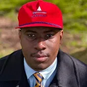 Red baseball cap with logo worn by a young man outdoors on a sunny day.