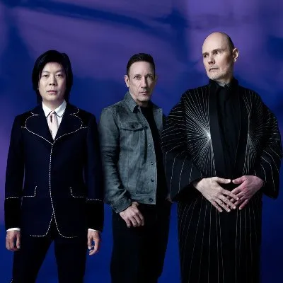 Elegant music group portrait featuring three diverse artists in artistic attire against a deep blue background.