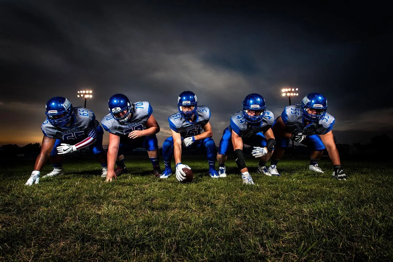 Team of American football players in blue uniforms preparing for game on a grassy field under evening sky.