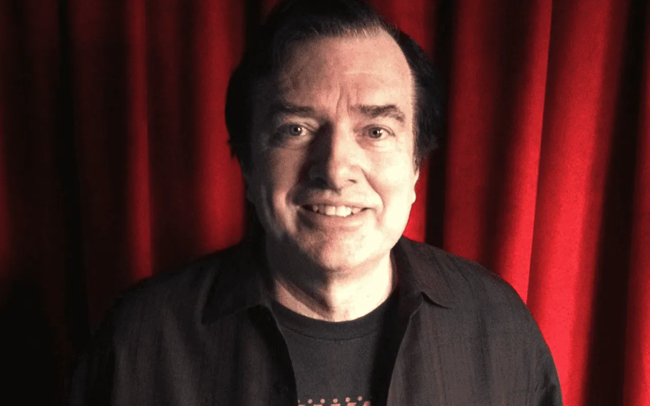 Photo of a man with dark hair smiling in front of a red curtain, music industry expert and keynote speaker at Hypebot events,