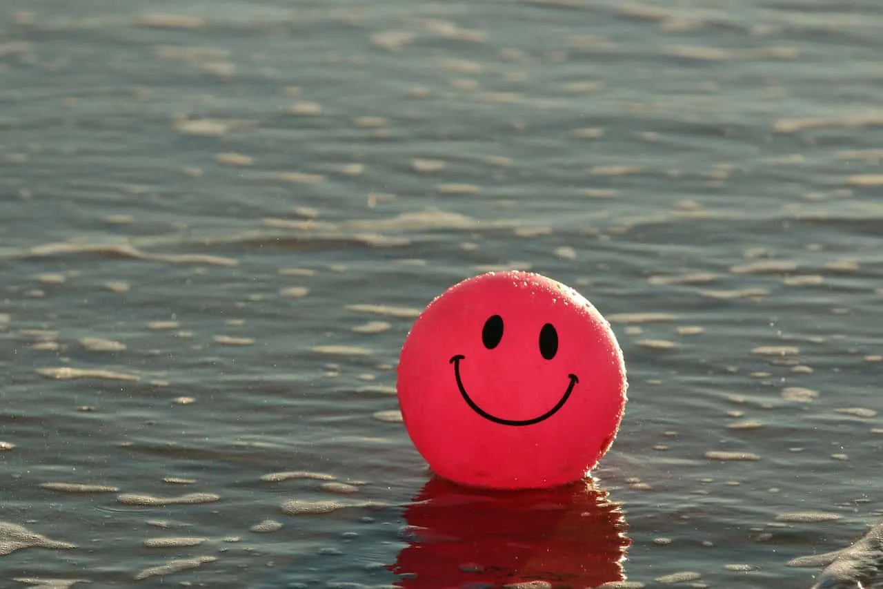 Bright pink smiling beach ball floating on calm ocean water, representing positivity and happiness, perfect for summer, leisu