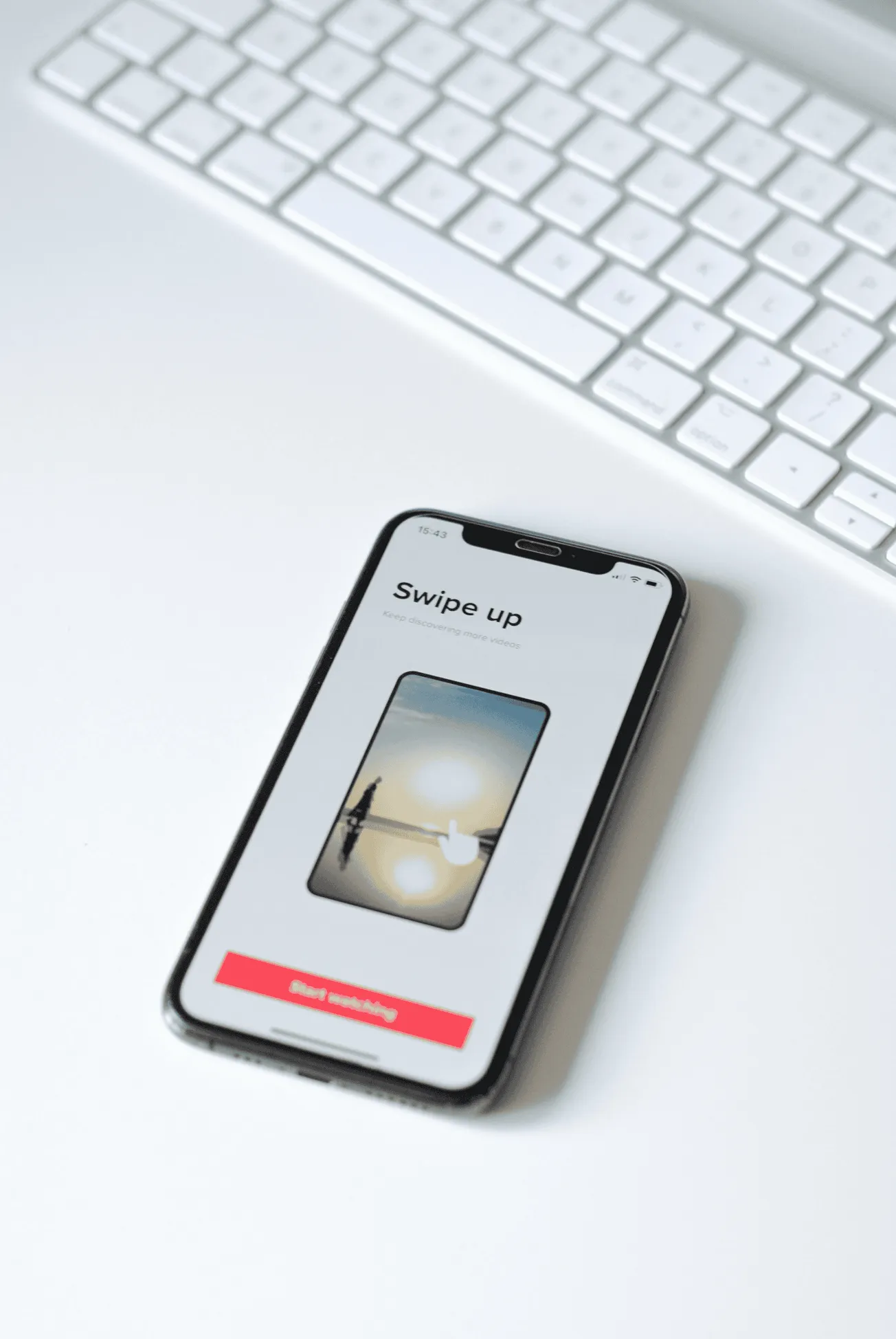Screenshot of a smartphone displaying a swipe-up video feature on a white desk with a keyboard in the background, illustratin