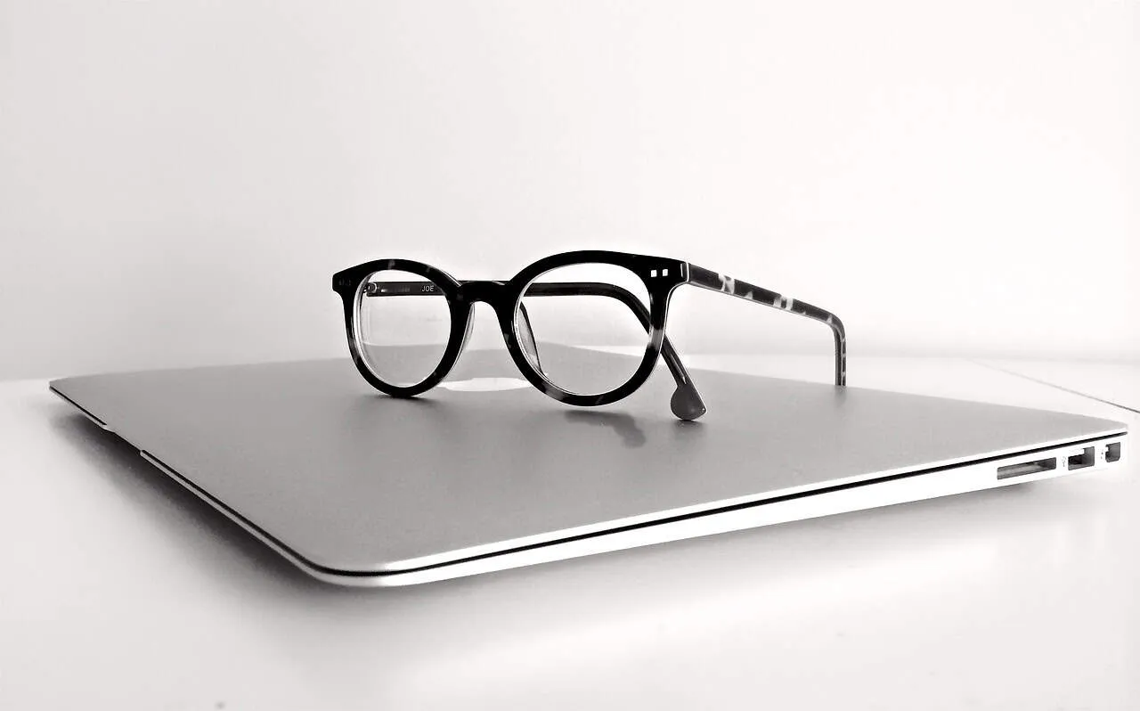 Black and white image of eyeglasses resting on a closed laptop, symbolizing technology and eyewear fashion.