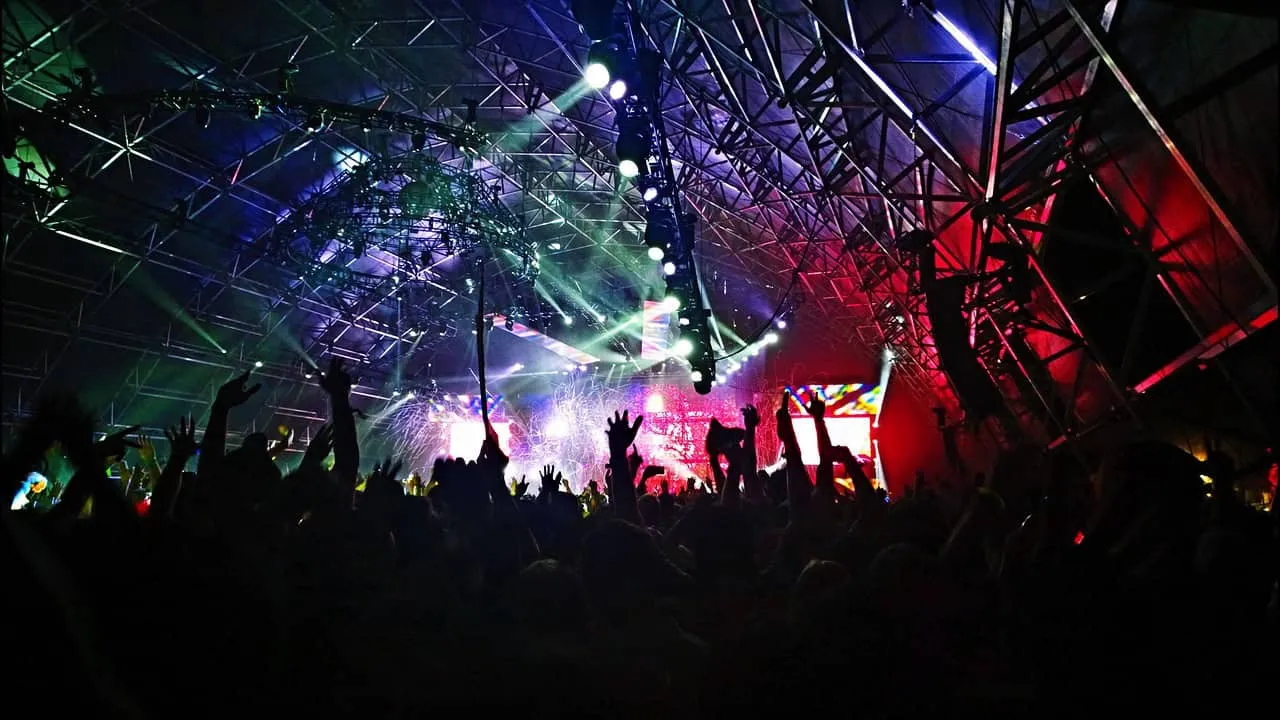 Vibrant concert stage with dynamic lighting, energetic crowd raising hands at a music festival or live performance, showcasin