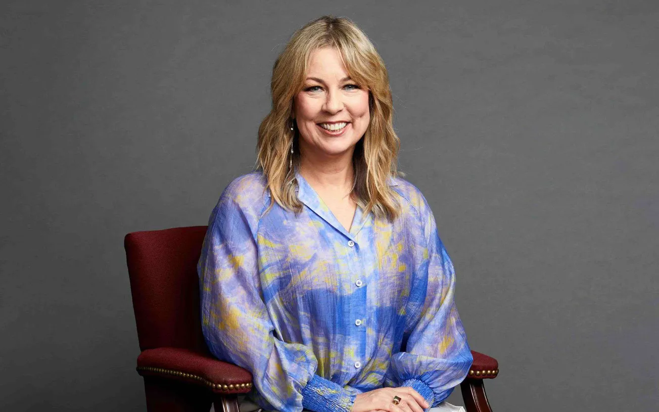 Bright smiling woman sitting on a red chair, wearing a colorful blue and yellow blouse with a gray background. Editorial port