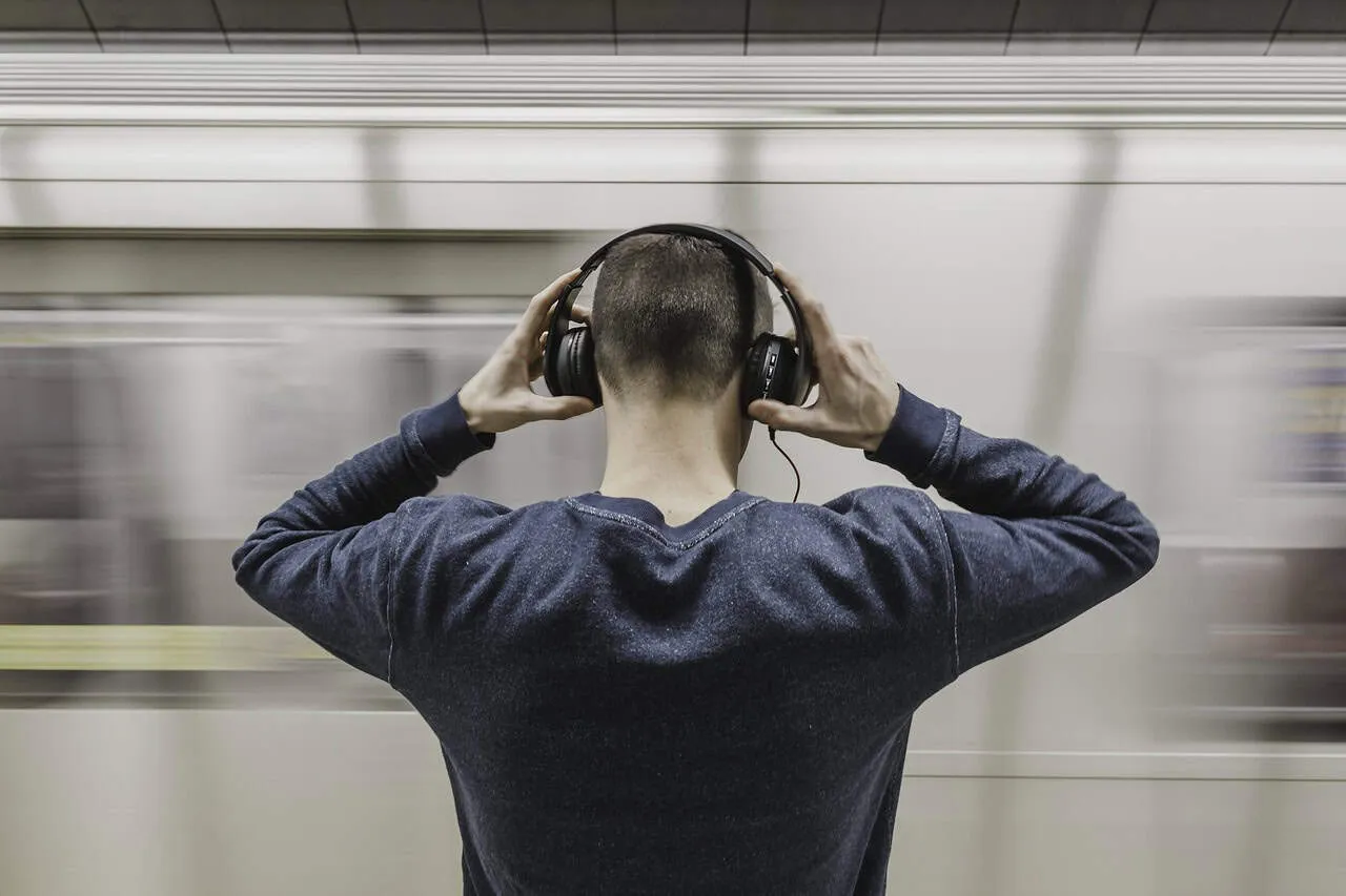 Headphones-wearing-man-on-subway-platform-listening-to-music-in-an-urban-setting-with-motion-blur-background.