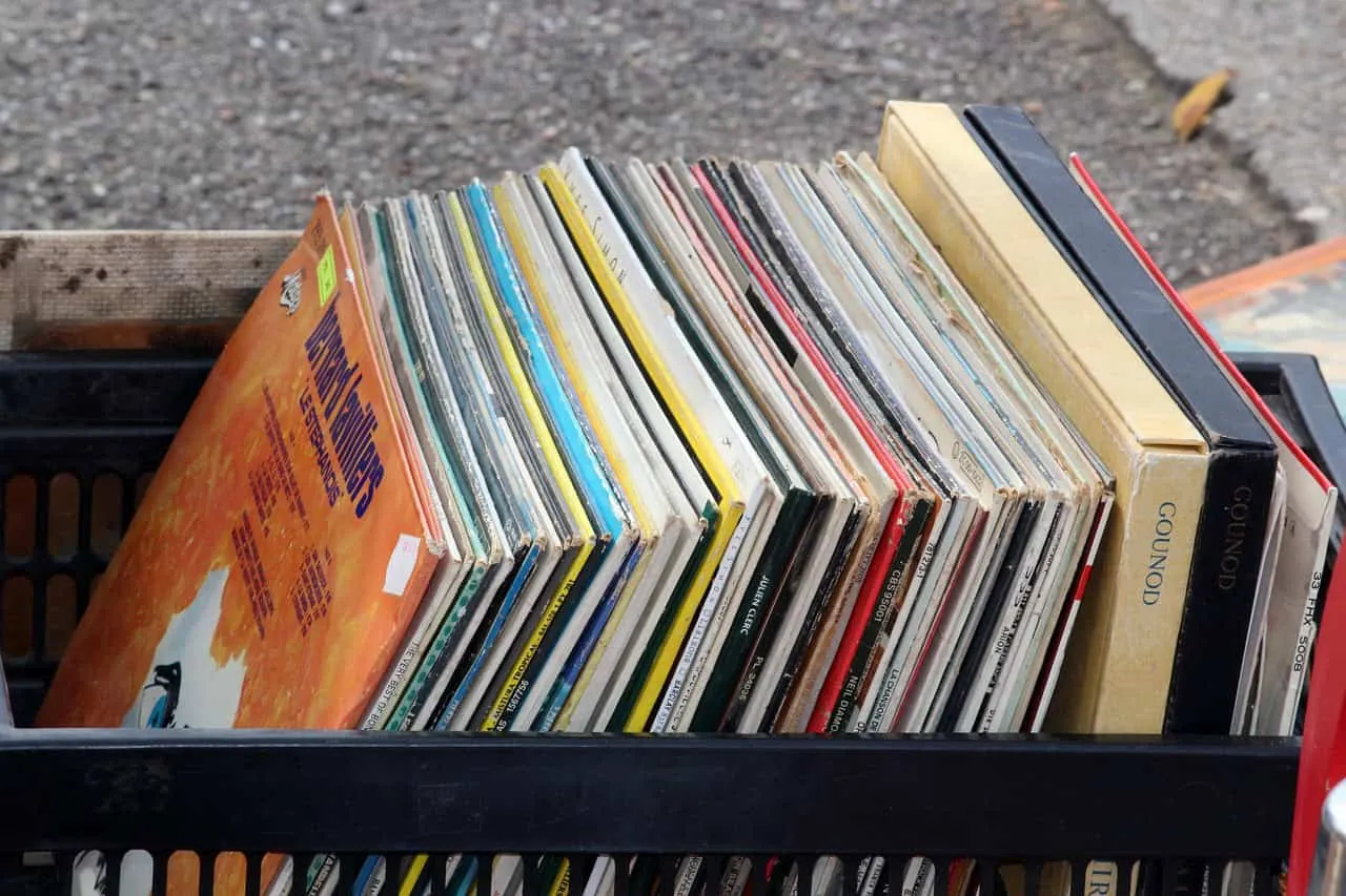 Magazines and vinyl records in a black crate, outdoor setting, vintage media collection, music and entertainment, eclectic co