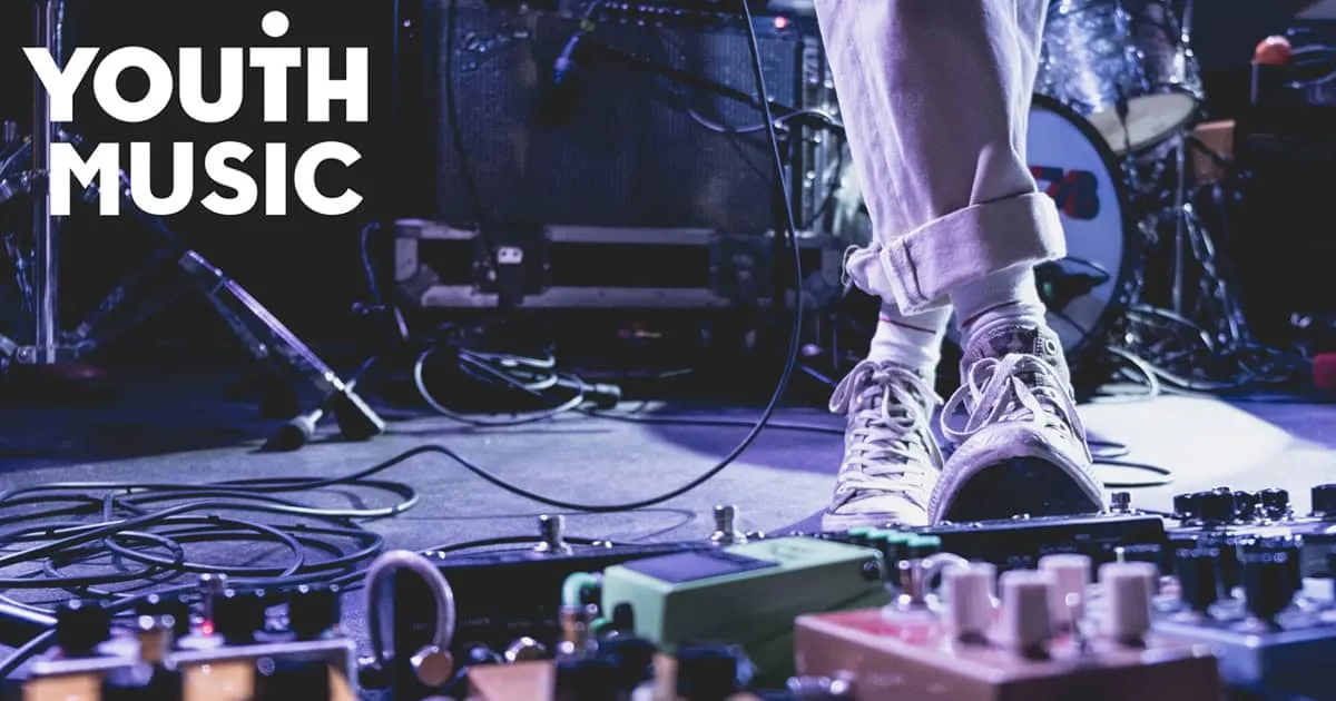 Performing youth musician on stage with guitar effects pedals and sound equipment, emphasizing youth music, live performance,