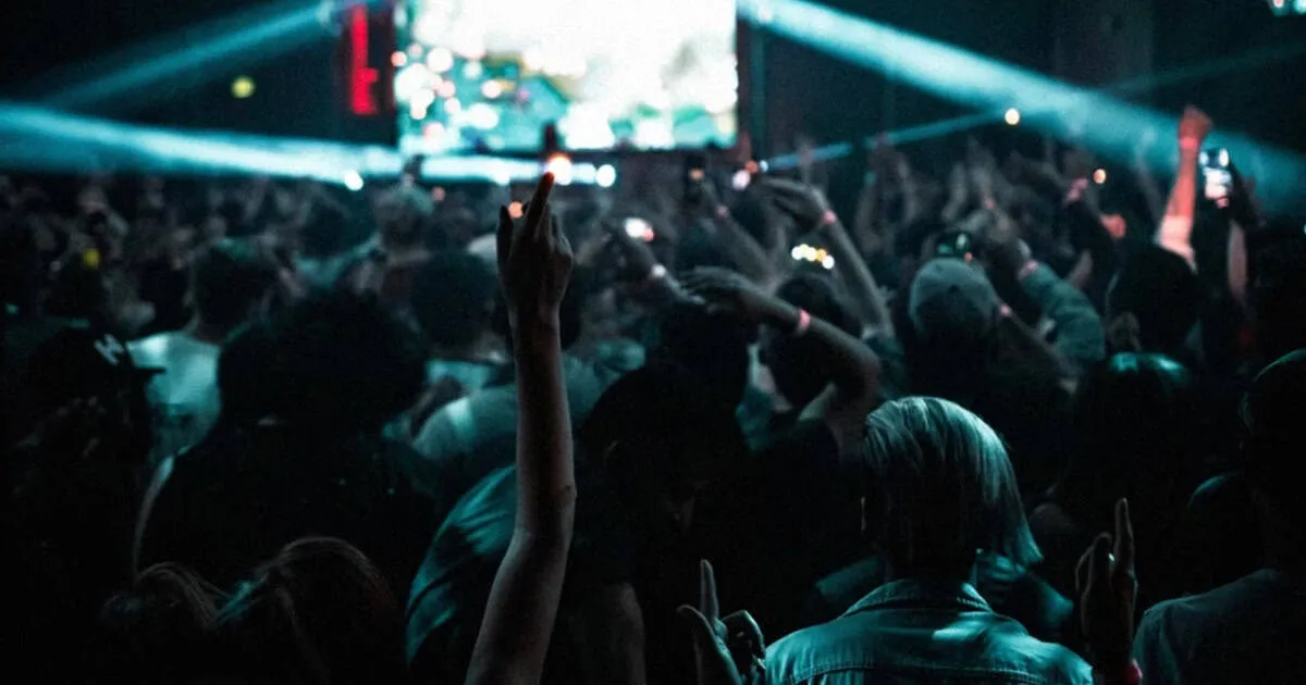 Vibrant concert crowd at a live music event with hands raised, colorful lights, and energetic atmosphere, capturing the essen
