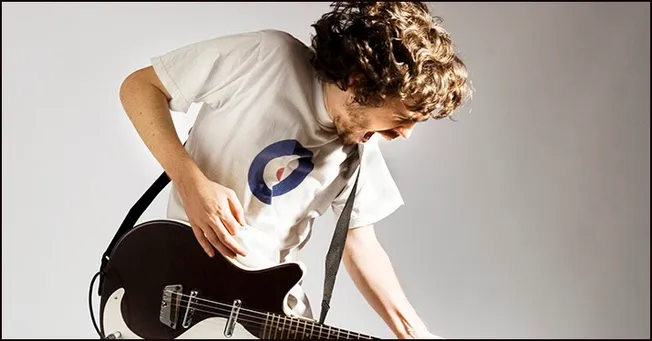 Guitarist playing guitar passionately, wearing a white t-shirt with a logo, engaging in music performance or practice.