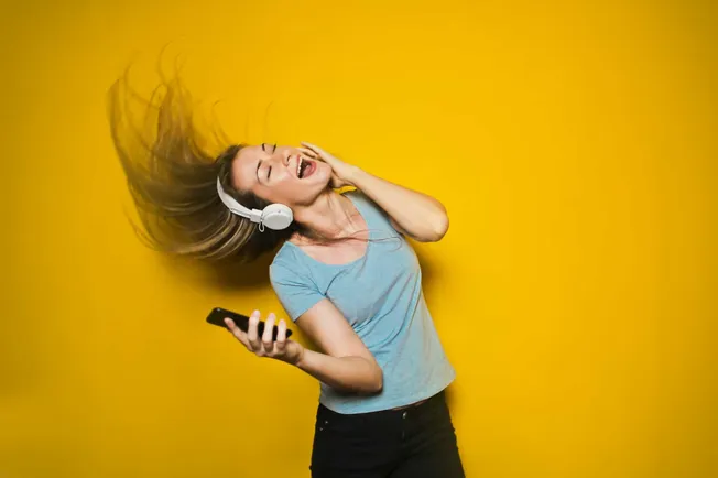Vibrant young woman enjoying music with headphones, dancing and smiling against bright yellow background, emphasizing music,