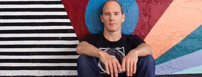 Stylish man sitting in front of vibrant, geometric street art mural, urban background with colorful painted wall, modern fash