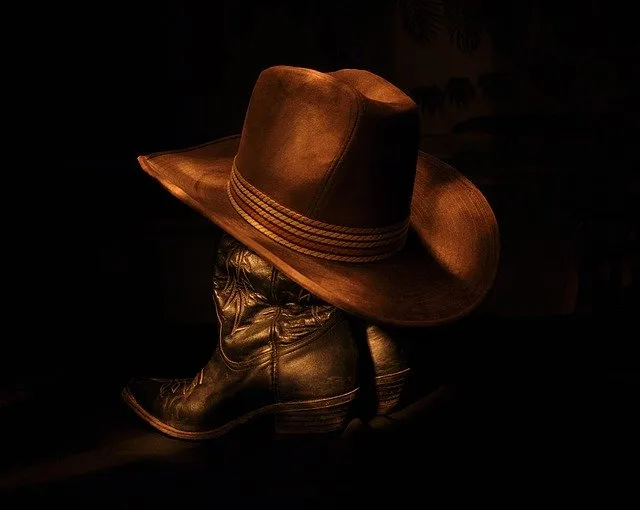 Cowboy boots with a wide-brimmed hat resting on top, dark background, Western wear style, rugged footwear, country fashion, o