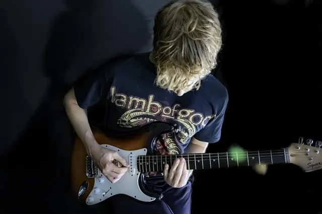 A young musician playing an electric guitar, wearing a "lambofgod" t-shirt, captured in a creative music-inspired environment