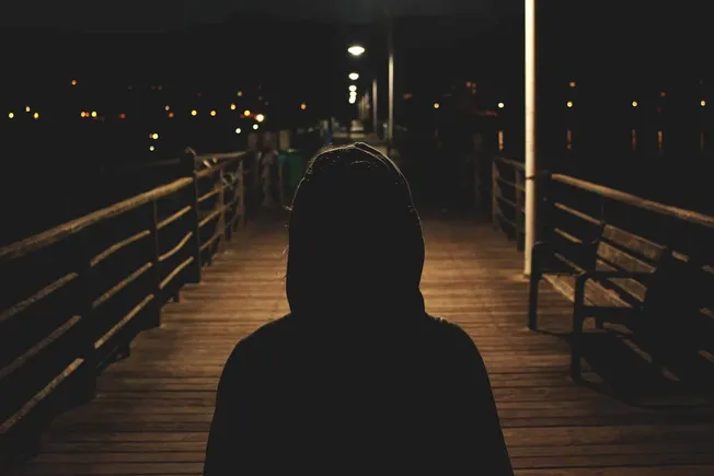 Silhouette of a person on a wooden pier at night with city lights in the background, illuminated by street lamps.