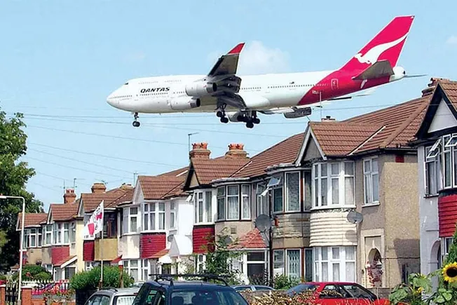 Qantas airplane flying low over residential neighborhood with houses and parked cars.