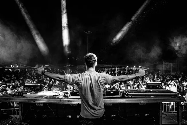 DJ performing at a lively music festival with a large crowd, stage lighting, and energetic atmosphere enhancement.