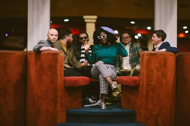 Bingo and six friends socializing in a stylish lounge with vintage decor, vibrant lighting, and a cozy atmosphere, enjoying a