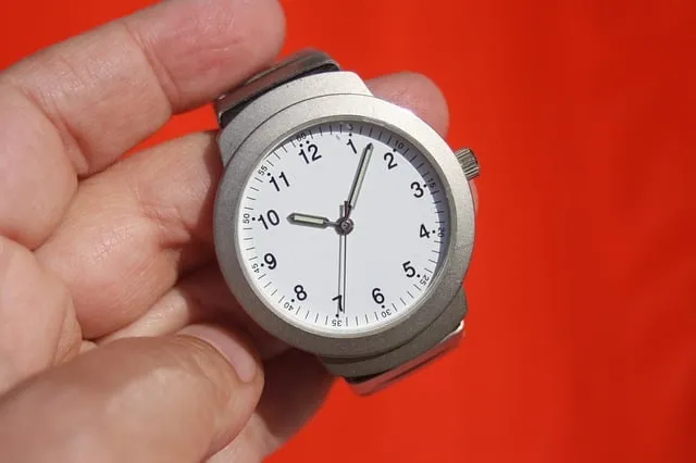 Vintage analog wristwatch showing 12:49, close-up on person's hand with red blurred background.