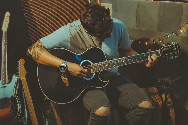 Young musician playing acoustic guitar in a cozy, decorated music studio.
