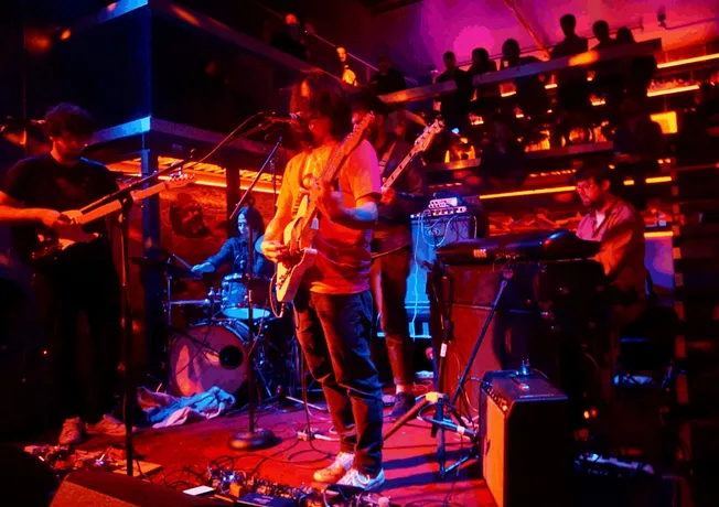 Dynamic live music performance featuring a band playing electric guitars, keyboards, and drums in a vibrant, colorful venue w