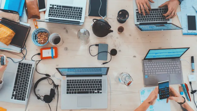 Laptops, smartphones, and digital devices on a wooden desk in a collaborative workspace for music industry professionals and