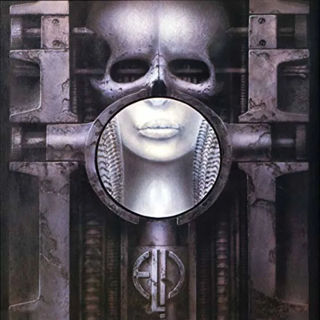 A futuristic metallic sculpture featuring a human face with a skull overlay, surrounded by industrial elements; representing