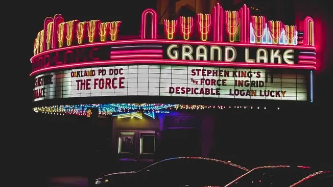 Grand Lake Theatre marquee illuminated with neon lights at night, showcasing upcoming film titles and showtimes. The classic