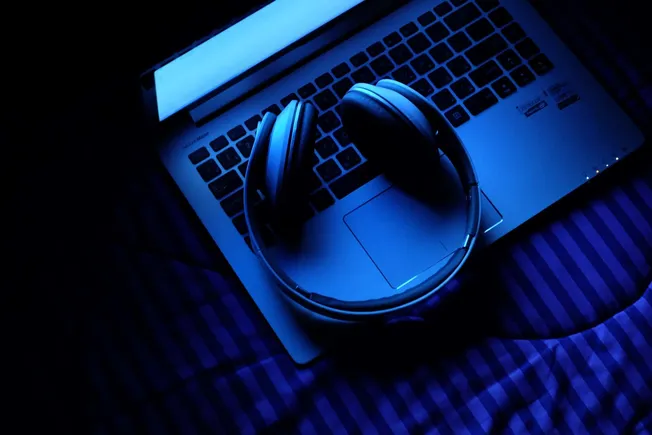 Wireless headphones resting on a laptop keyboard with a blue glow, capturing the essence of music and digital media technolog
