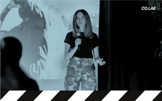 Woman giving presentation at tech conference or workshop, young female speaker with microphone, casual clothing, urban enviro