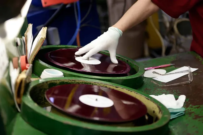 Vinyl record manufacturing process with a worker inspecting a spinning record on a green turntable, emphasizing music product