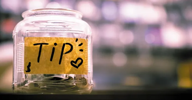 Tips jar with handwritten "TIP" note and heart, for saving and collecting gratuities or advice, in a casual environment.