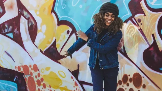 Colorful graffiti wall with smiling young woman enjoying urban street art, showcasing creativity and modern culture.