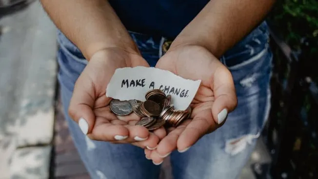 Coins in hands with a note saying "Make a Change" for social impact and fundraising.