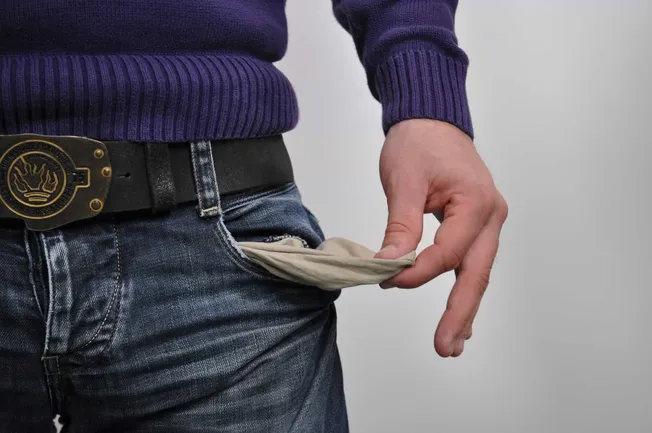 Discarded empty beige wallet slipping out of pocket, man wearing casual denim jeans and purple sweater, emphasizing financial