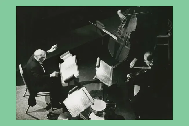 Elderly classical musicians performing a duet with a piano and violin on stage during a concert.