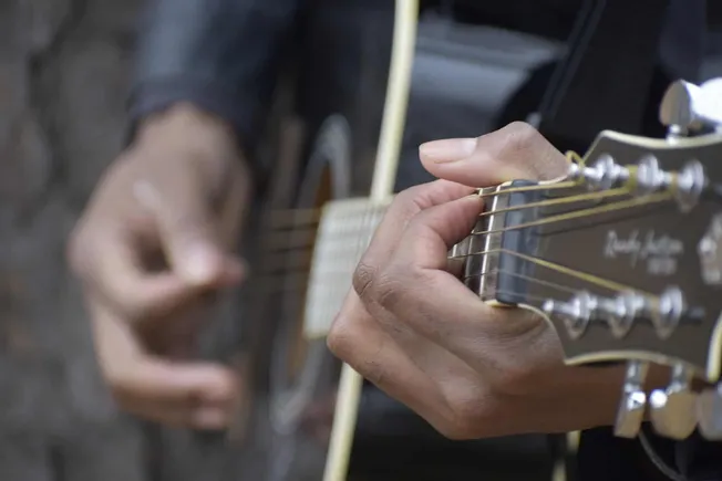 Acoustic guitar player hand close-up, focusing on fingers pressing strings on fretboard, live music performance, musician pla