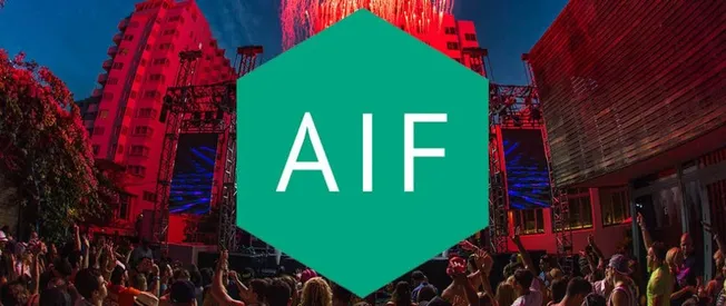 AIF logo at an outdoor music festival with a large crowd, stage, and modern buildings in the background, showcasing live elec