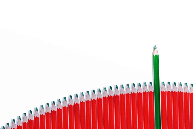Bright red and green colored pencils forming a rising bar chart with one green pencil standing taller, symbolizing growth, cr