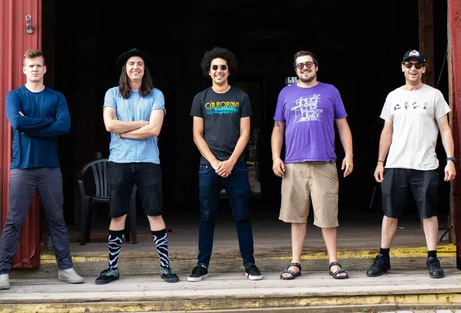 Someone standing on a wooden porch of a building with five other individuals, all casually dressed, smiling and posing for a