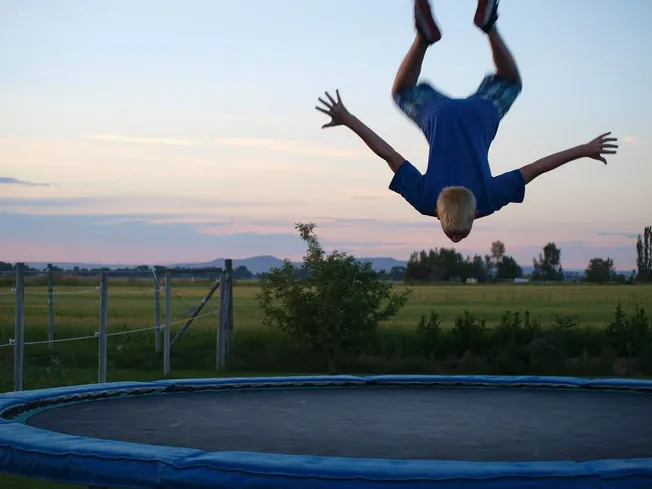 Child jumping on trampoline outdoors at sunset, backyard setting, playful and energetic moment, summer evening, kids activity