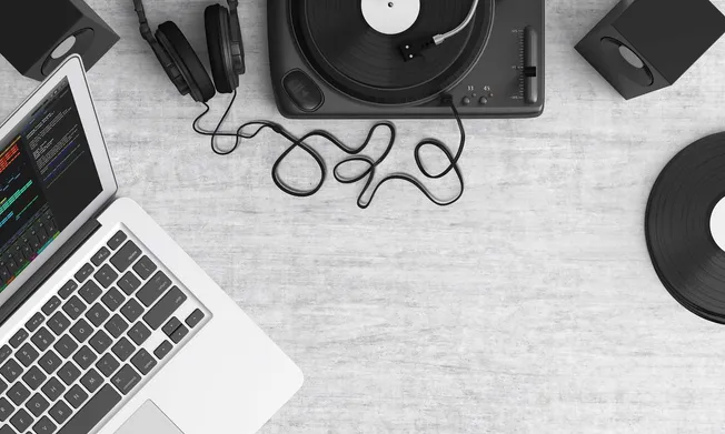 Headphones, DJ turntable, and laptop setup on a wooden surface for music production or digital music marketing.