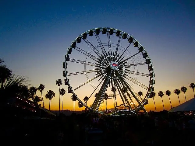 Ferris wheel at sunset during a music festival, with palm trees and tents in the background, capturing a lively outdoor event